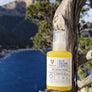 Olio solare protettivo per capelli 100% di ingredienti naturali 100% biodegradabile. flacone in pet trasparente da 100ml, immagine di prodotto poggiato su un ginepro al mare del golfo di Orosei