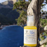 Olio solare protettivo per capelli 100% di ingredienti naturali 100% biodegradabile. flacone in pet trasparente da 100ml, immagine di prodotto poggiato su un ginepro al mare del golfo di Orosei