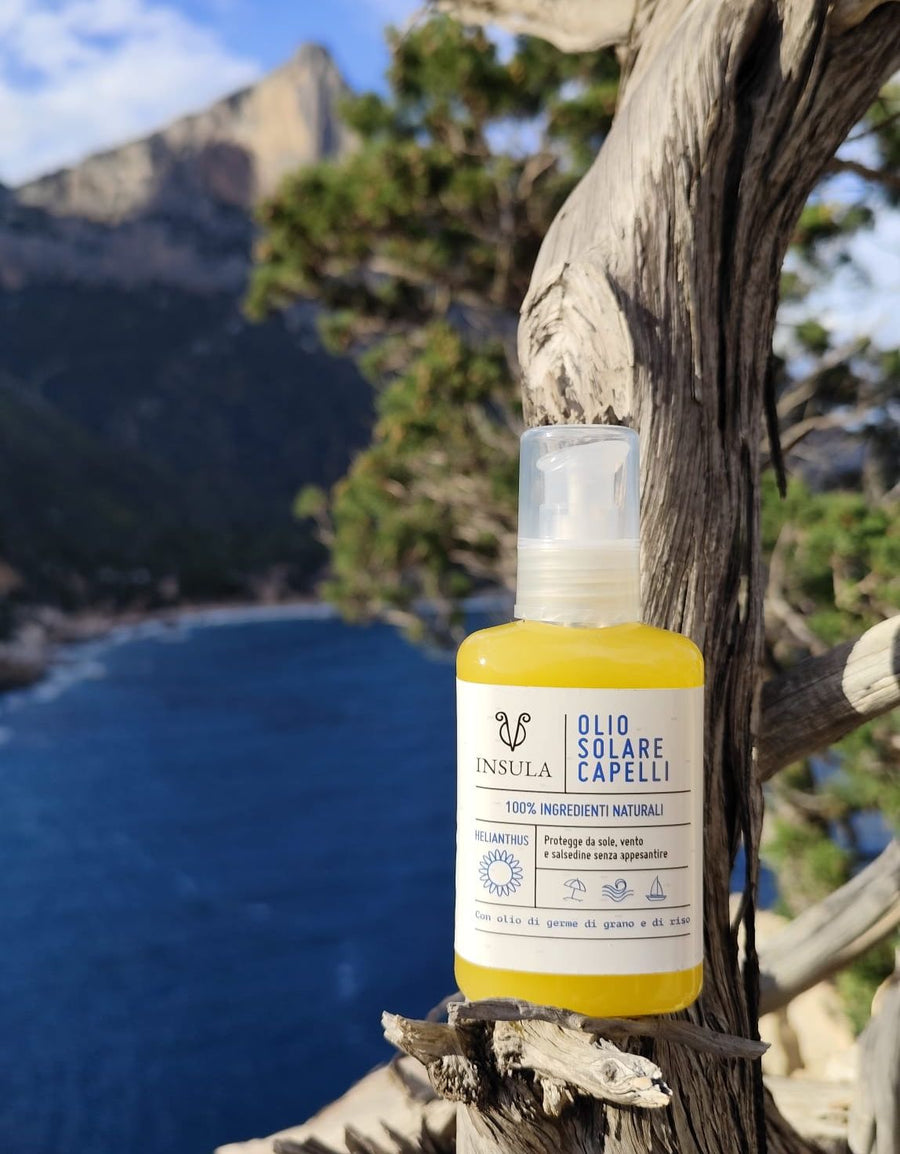 Olio solare protettivo per capelli 100% di ingredienti naturali 100% biodegradabile. flacone in pet trasparente da 100ml, immagine di prodotto poggiato su un ginepro al mare del golfo di Orosei